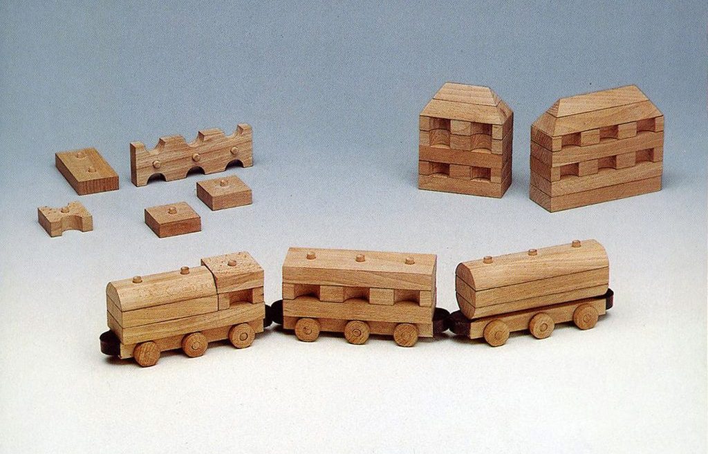 Drewniane modułowe zabawki, z przodu lokomotywa i wagony, w tle domy i pojedyncze klocki