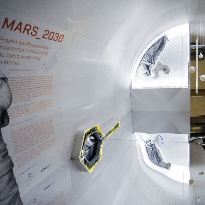 przestrzeń wystawy w kształcie białego tunelu z lustrzaną podłogą, na ścianie pomarańczowy napis MARS 2030 oraz mniejsze teksty informacyjne