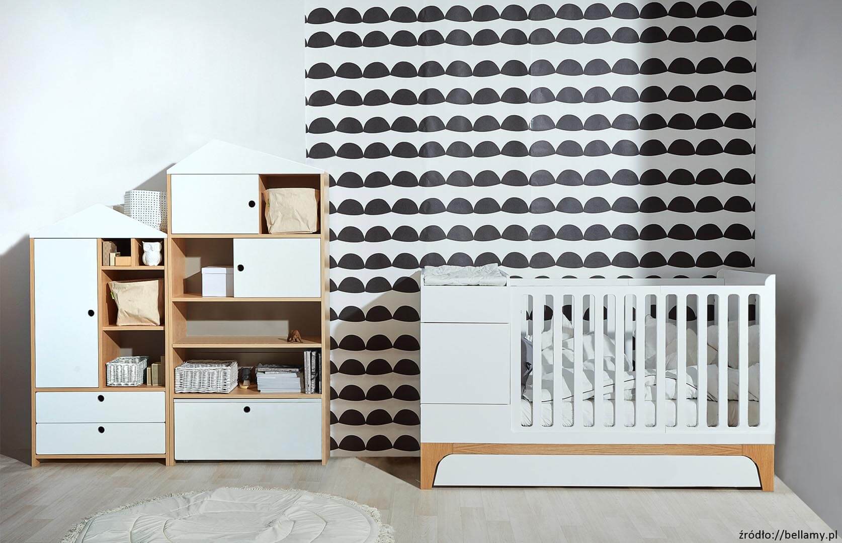 pokój dziecięcy a w nim zestaw mebelków: biała komoda z szufladami i półkami oraz białe łóżeczko dziecięce. W tle mocna graficzna tapeta