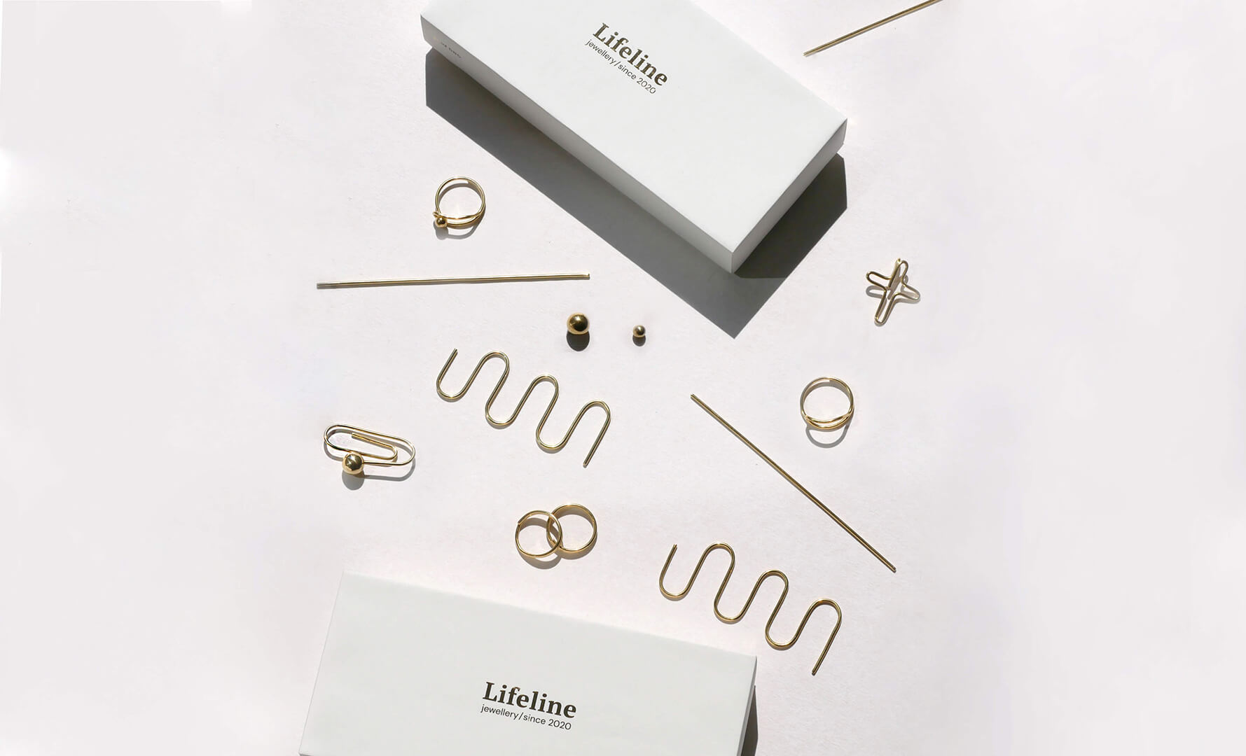 Złota biżuteria rozłożona na białym podłożu. Obok białe pudełka ze złotym napisem Lifeline Jewellery since 2020